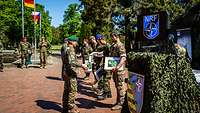 Zertifizierung gelungen Auf einem Platz stehen Soldaten nebeneinander, zwei Soldaten vor ihnen überreichen Urkunden.