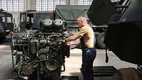 Ein Soldat schraubt an einem Motorblock in einer Halle