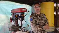 Ein Soldat in einer Werkstatt, lacht in die Kamera