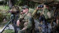 Drei Soldaten beobachten aus einem Versteck die Einschläge der Artilleriegranaten.