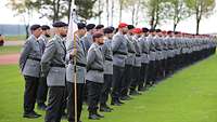 Zahlreiche Soldaten stehen in Formation auf einer Wiese. Ein Soldat hält einen weißen Wimpel.