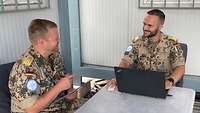 Oliver B. sitzt mit einem anderen Soldaten an einem Tisch und arbeitet an einem Laptop, während sich die beiden unterhalten