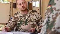 Ein Soldat sitzt in Uniform am Tisch und macht sich Notizen