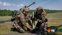 Zwei Soldaten setzen Munition zusammen, im Hintergrund steht ein Geschütz.