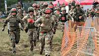 Soldaten mit roten Nummern an Helmen und Uniform rennen bei einem Sportwettkampf um die Wette.