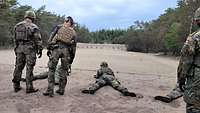 Mehrere Soldaten liegen schießend mit dem Gewehr auf Sandboden. Dahinter steht die Aufsicht.