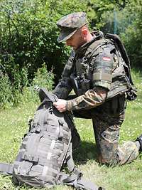 Ein Soldat packt einen Rucksack auf einer grünen Wiese