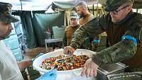 Ein Soldat bereitet den Salat in einer großen Schüssel vor und wird dabei von einem Kameraden unterstützt