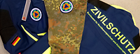 Eine Bundeswehr Uniform und eine Jack vom Zivilschutz die übereinander liegen beide mit dem Zeichen des BBK