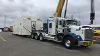 Transport SARah-Satellit mit US-Truck Ein amerikanischer Lieferwagen steht zusammen mit einem großen weißen Container in einer Hafenanlage
