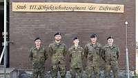 Vier Soldaten und eine Soldatin stehen in Feldanzug vor einer Hauswand
