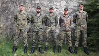 Fünf Soldaten stehen in Feldanzug vor einer Steinmauer