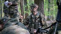 Ein Soldat mit Tarnfarbe im Gesicht während der Befehlsausgabe im Wald