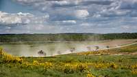 Bis an das Gefecht ran In der Ferne über die offene Heide fahren mehrere hintereinander Lkw, Staub wirbelt auf.