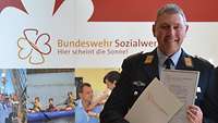 Ein Soldat steht vor einer Wand mit dem Text "Bundeswehr Sozialwerk - Hier scheint die Sonne!"
