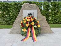 Im Gedenken Stein mit Eisernem Kreuz davor ein Blumenkranz mit schwarz-rot-goldenen Schleifen