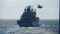 Ein graues Schiff und ein Hubschrauber üben miteinander.