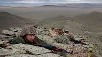Zwei mongolische Soldaten liegen mit Gewehr auf Felsen in einer Steppe.