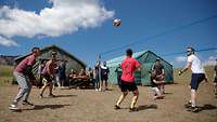 Vor zwei Zelten spielen mongolische und deutsche Soldaten in Sportkleidung Volleyball.