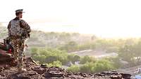 Ein Soldat steht im Kampfanzug im Morgenlicht auf einem Berg und schaut auf den am Camp vorbeifließenden Niger.