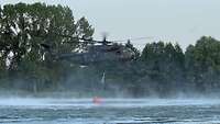 Ein Hubschrauber der Bundeswehr schöpft Wasser aus einem See. 