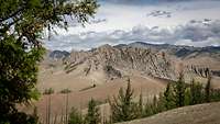 Landschaft mit schroffen, zerklüfteten Felsformationen. Im Vordergrund stehen Nadelbäume.