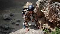 Ein mongolischer Soldat klettert auf felsigem Untergrund einen Berg hinauf.