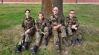 Zwei Soldatinnen und zwei Soldaten sitzen in Feldanzug vor einem Baum