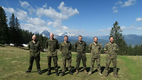 Sechs Soldaten stehen in Feldanzug auf einer Wiese im Hintergrund sind Berge zu sehen