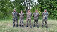 Fünf Soldaten stehen im Feldanzug auf einer Wiese mit Bäumen im Hintergrund