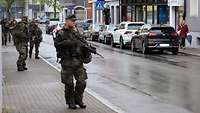 Mehrere Soldaten laufen mit ihrem Gewehr Patrouille auf dem Gehweg durch eine Stadt.