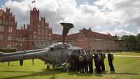 Eine Gruppe uniformierter Menschen an einem gelandeten Hubschrauber auf einer Wiese