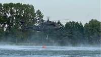 Ein Hubschrauber nimmt Wasser mittels einem fünftausend Liter Wasserbehälters auf.