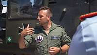 Berufswechsler innerhalb der Bundeswehr Ein Pilot in Fliegerkombi steht vor einem Hubschrauber und gestikuliert.