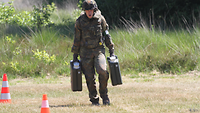 Ein Soldat in Feldanzug mit Helm und Weste trägt zwei Kanister