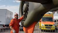Soldat im orangenen Fliegeranzug bei einem Heckrotor eines Rettungshubschraubers