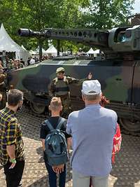 Ein Soldat steht vor einem Panzer. Zuschauer stehen um ihn herum.