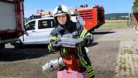 Am Hydranten Eine junge Feuerwehrfrau in Uniform und Schutzhelm dreht auf einem Flugplatz einen Wasser-Hydranten auf