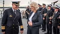 Ein Admiral in dunkelblauer Uniform neben einer Frau im grauen Hosenanzug.