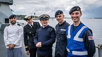 Fünf Marinesoldaten in unterschiedlichen Uniformen auf dem Oberdeck eines grauen Kriegsschiffs.