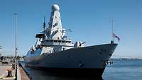 Ein großes graues Kriegsschiff neben einer Hafenpier.