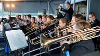 Blechbläser in dunkelblauer Marineuniform spielen unter einem grauen Zeltdach.