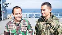 Ein indonesischer und ein mexikanischer Marineoffizier befinden sich auf einem Kriegsschiff und blicken in die Kamera.