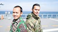 Ein indonesischer und ein mexikanischer Marineoffizier befinden sich auf einem Kriegsschiff und blicken in die Kamera.