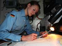 OL Tanja Müller am Arbeitsplatz Ein weiblicher Marineoffizier sitzt an einer Seekarte und zeichnet eine Route ein.
