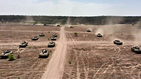 Auf einem weiten sandigen Areal fahren viele Panzer in Formation.