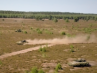 Puma-Angriff von oben Mehrere Panzer fahren mit hoher Geschwindigkeit über ein weites braunes Feld in der Sommerhitze.