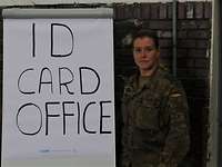 Eine Soldatin steht neben einem Schild mit der Aufschrift „ID Card Office“