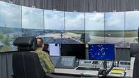 Zwei Soldaten sitzen in einem Raum mit vielen Monnitoren auf denen ein Flugplatz abgebildet ist