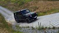 Eine Mercedes G-Klasse in der militärischen Variante „Greenliner“ fährt eine Steigung hinauf. Der Untergrund wechselt.